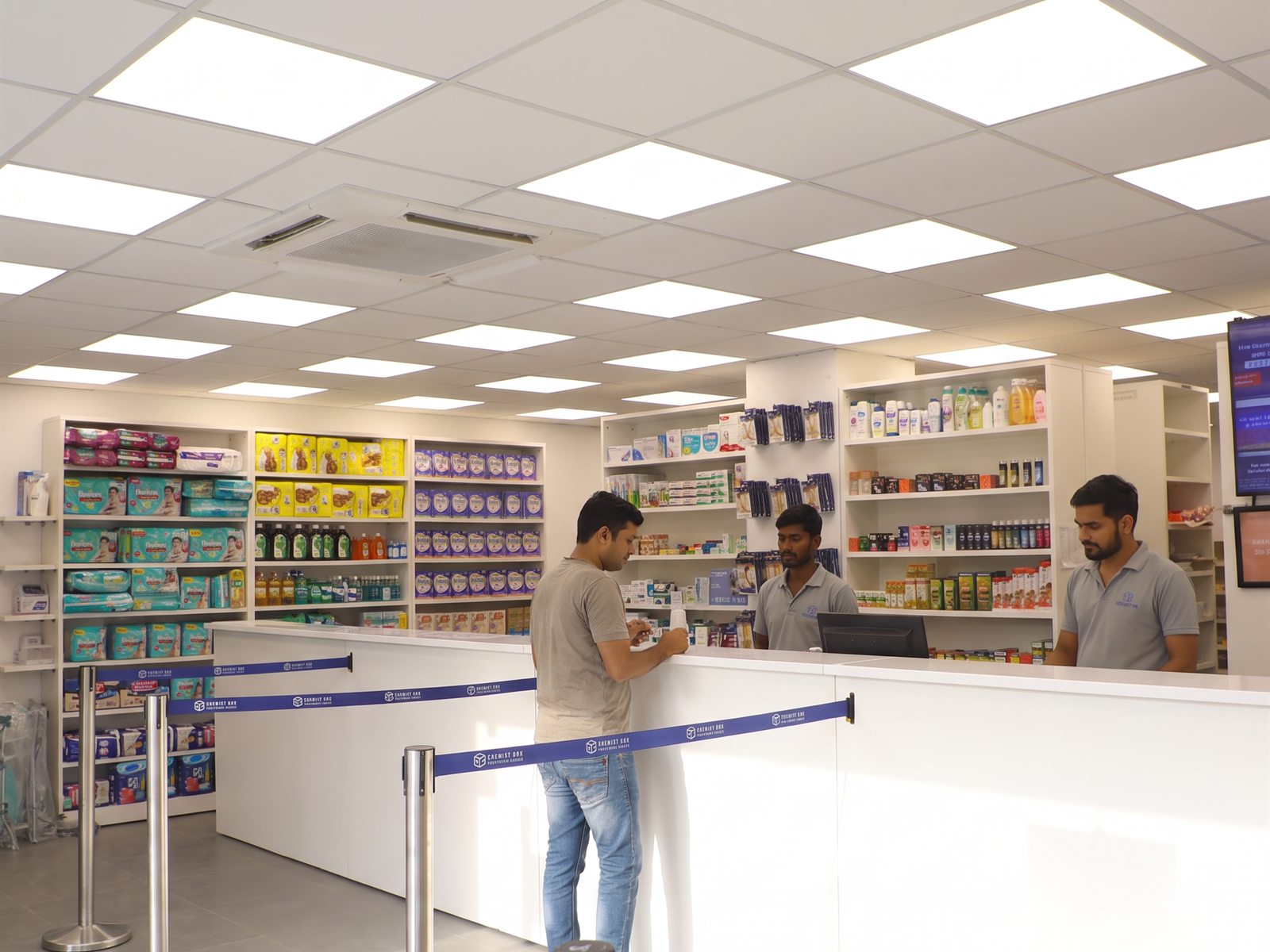 Brightly lit, fully stocked medicine shelves at a Chemist Box store with digital pricing screen